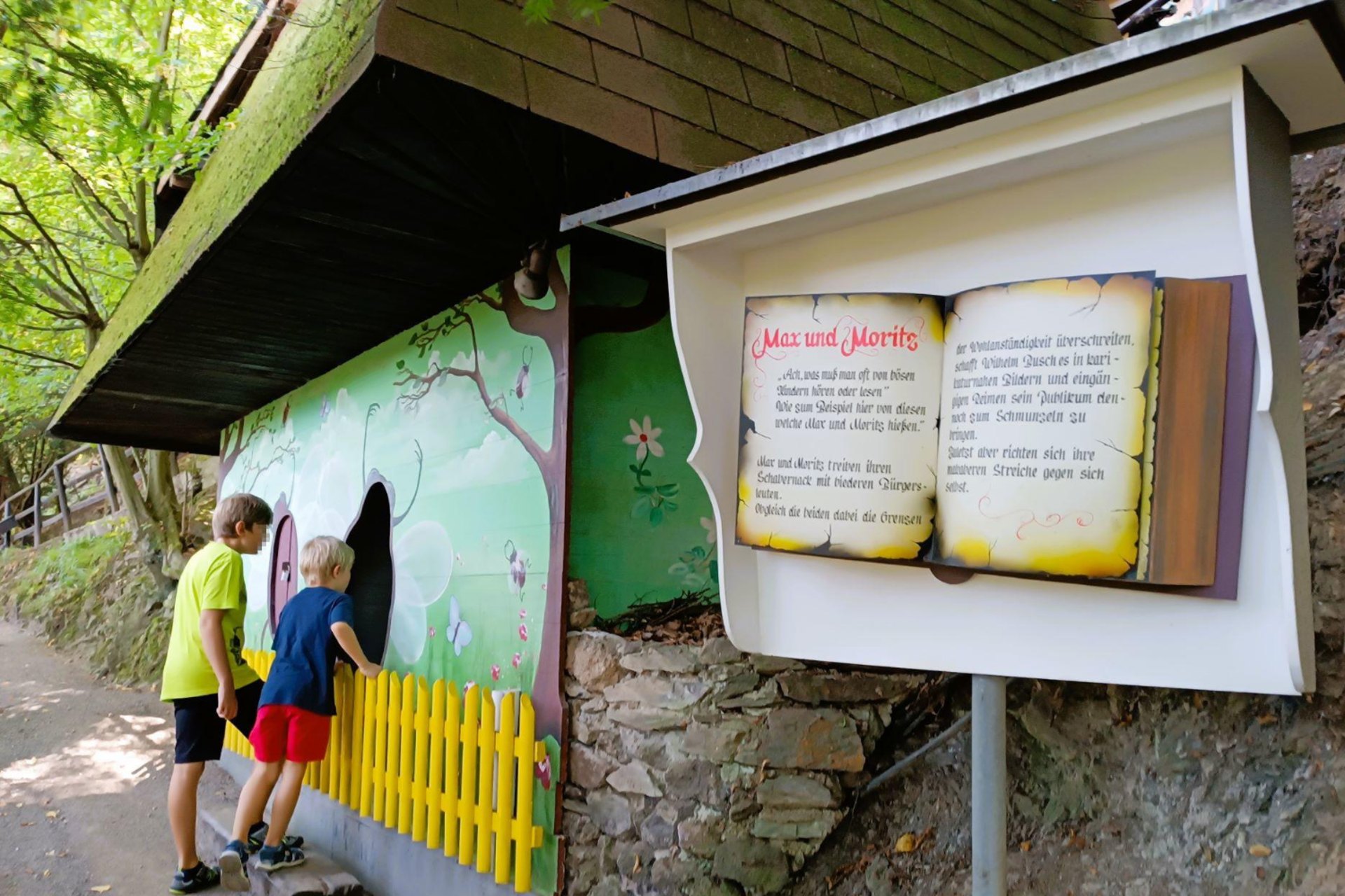 Zwei Kinder an der Station „Max und Moritz“ neben der aufgeschlagenen Erzähltafel